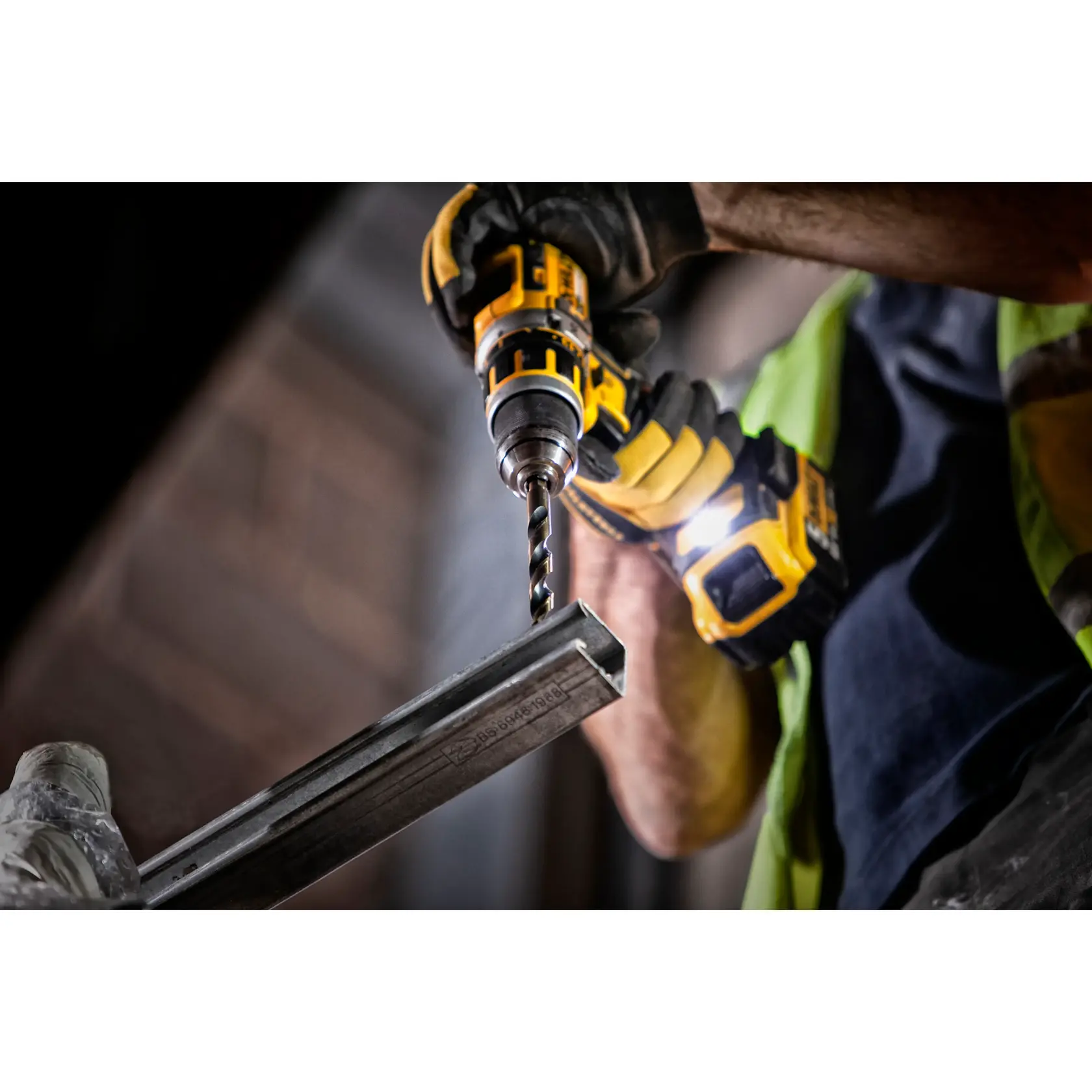 Person drills into metal with yellow DEWALT power tool, wearing gloves. Close-up, industrial setting.