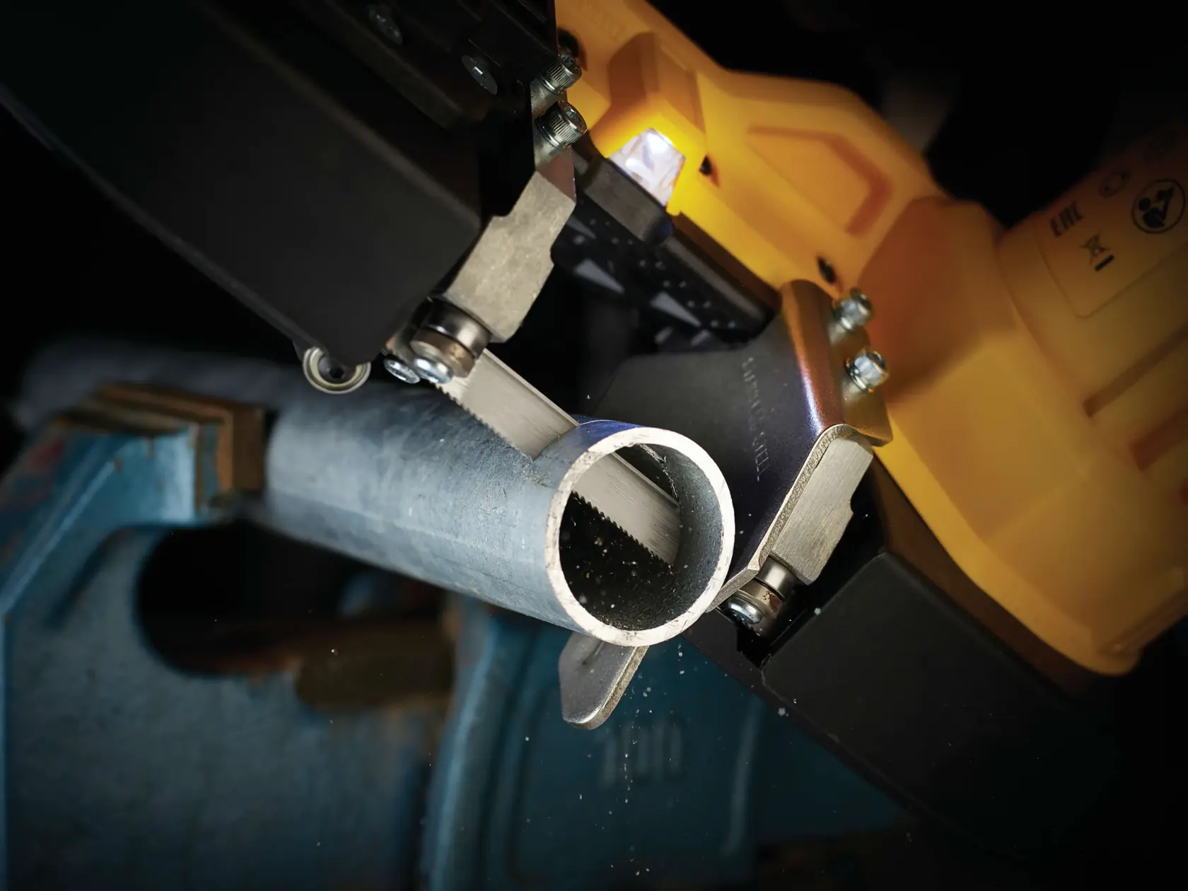 Close-up of a DEWALT saw cutting a metal pipe held in a vise.
