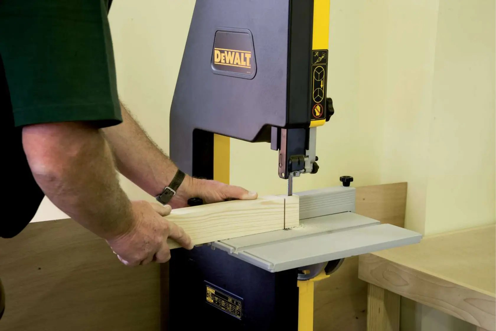 Person operating DEWALT bandsaw to cut wood in a workshop setting.