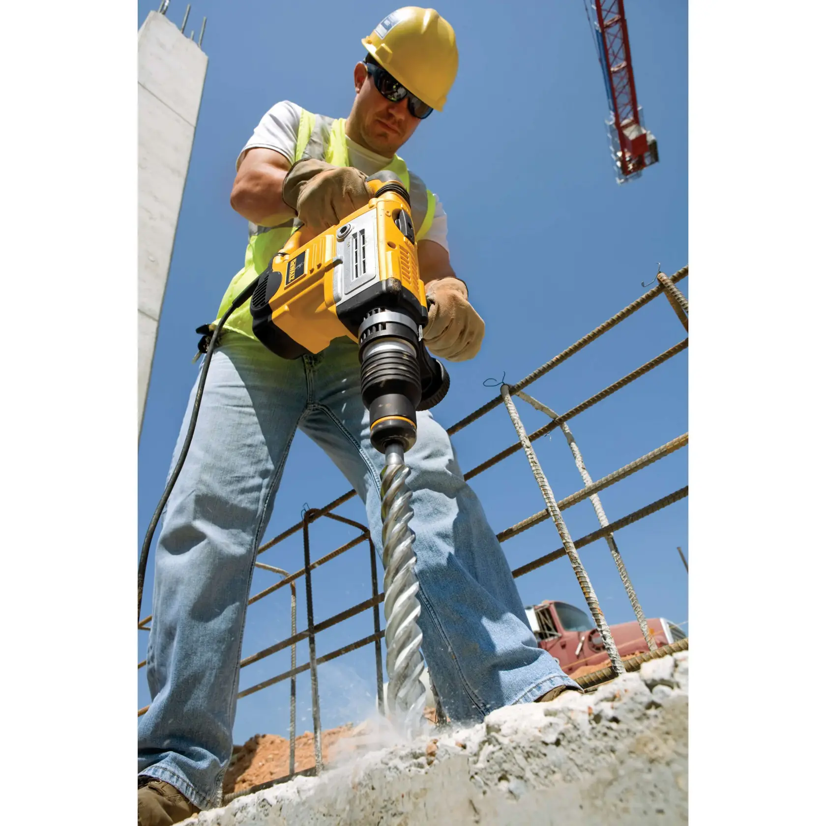 Worker uses DEWALT drill to bore into concrete at a construction site, wearing safety gear and gloves.