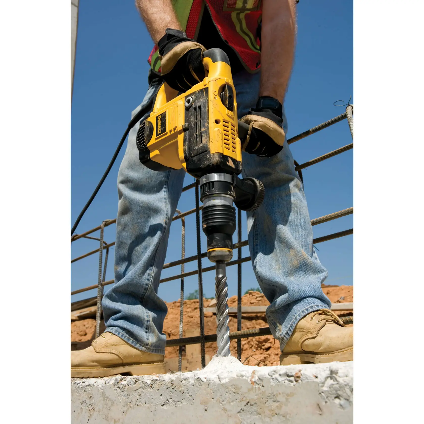 Person using a yellow DEWALT drill to bore into concrete at a construction site.
