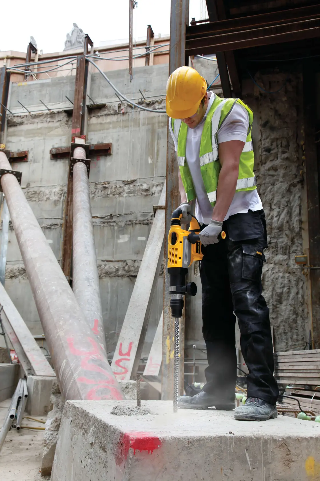 Photo of worker using DEWALT rotary hammer DT9450 to drill into concrete block at construction site.