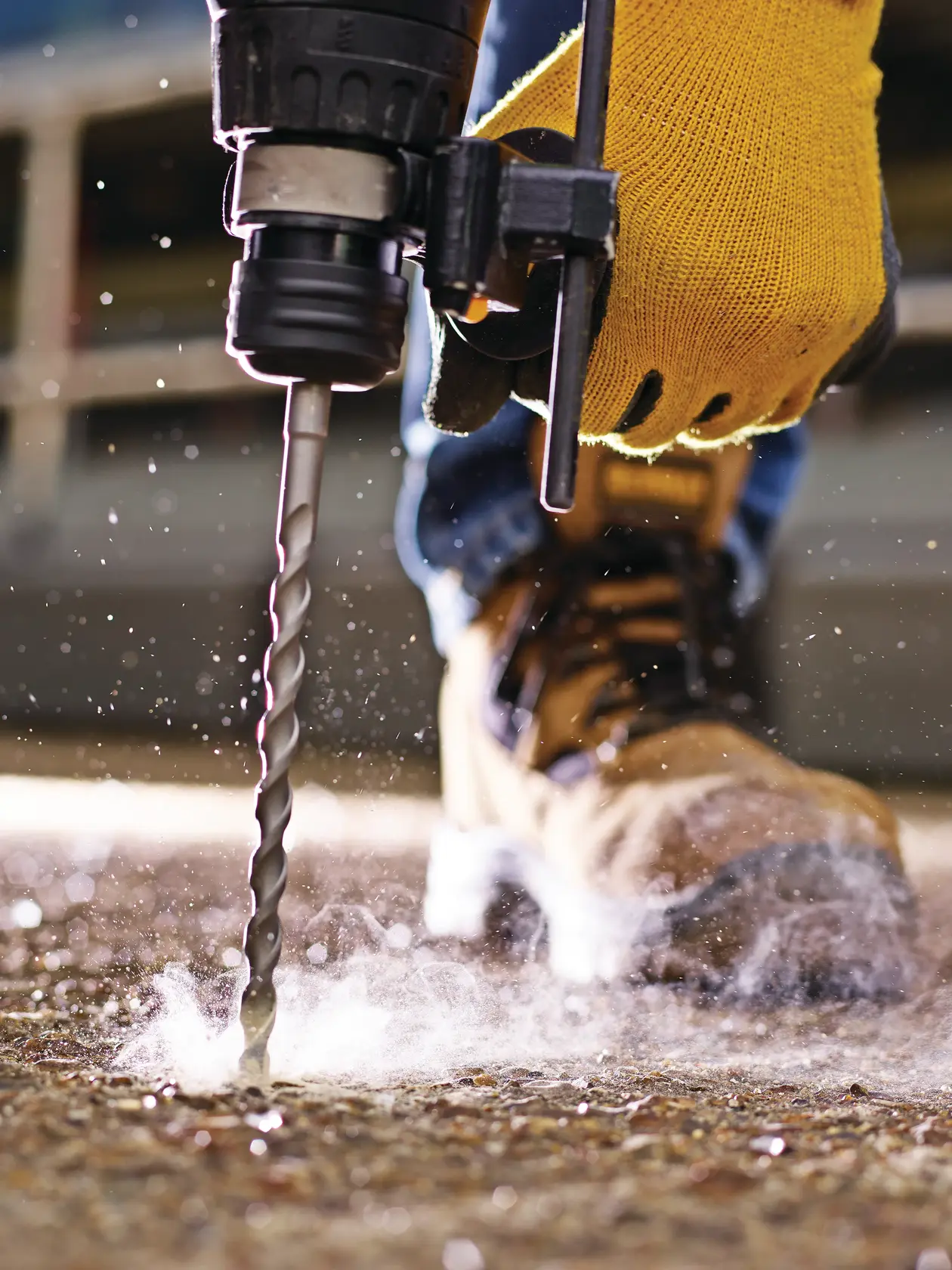 Photo of DEWALT DT9524 drill bit in use on concrete by worker with gloves, close-up action shot.