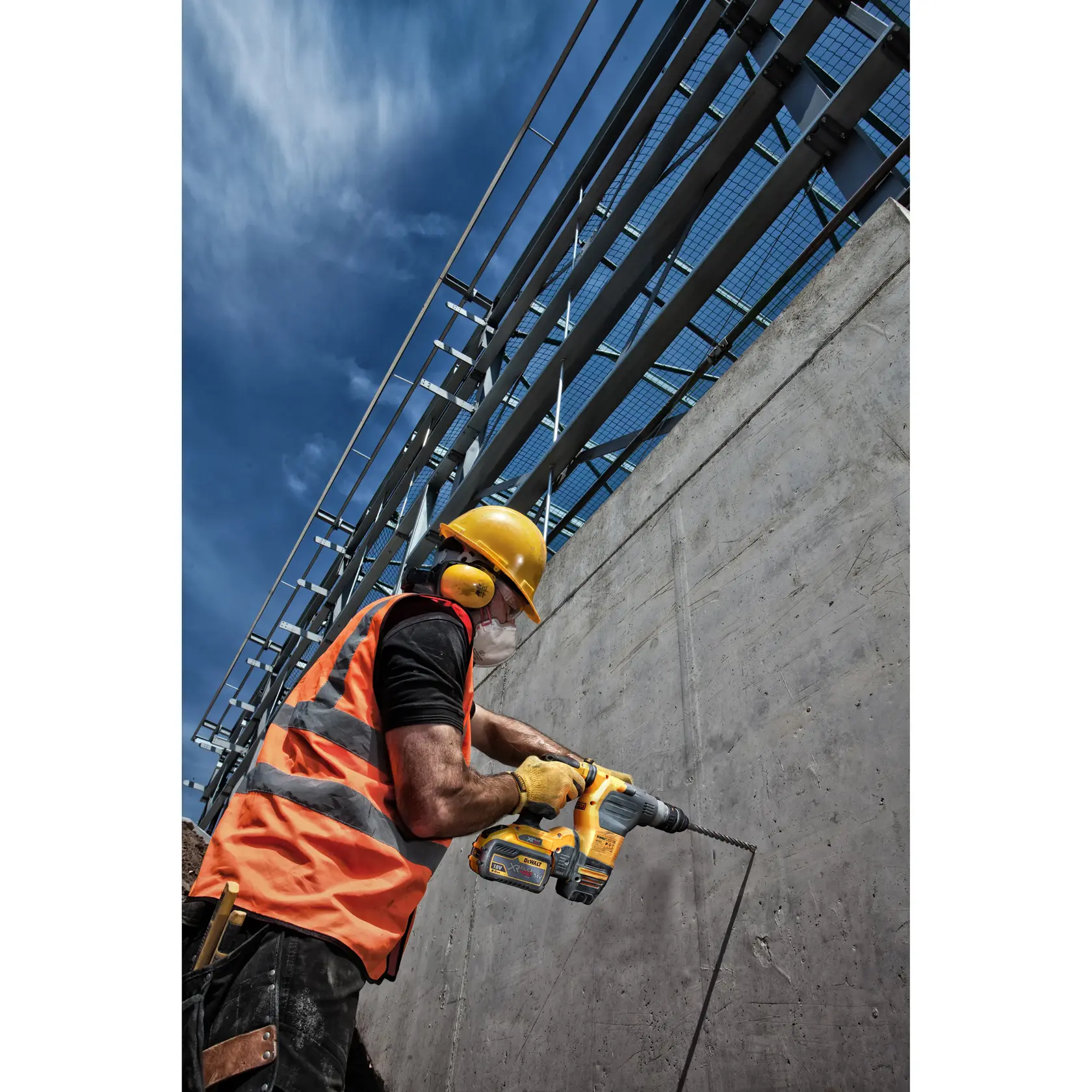Trabajador perfora pared de concreto con taladro DEWALT inalámbrico, lleva equipo de seguridad.
