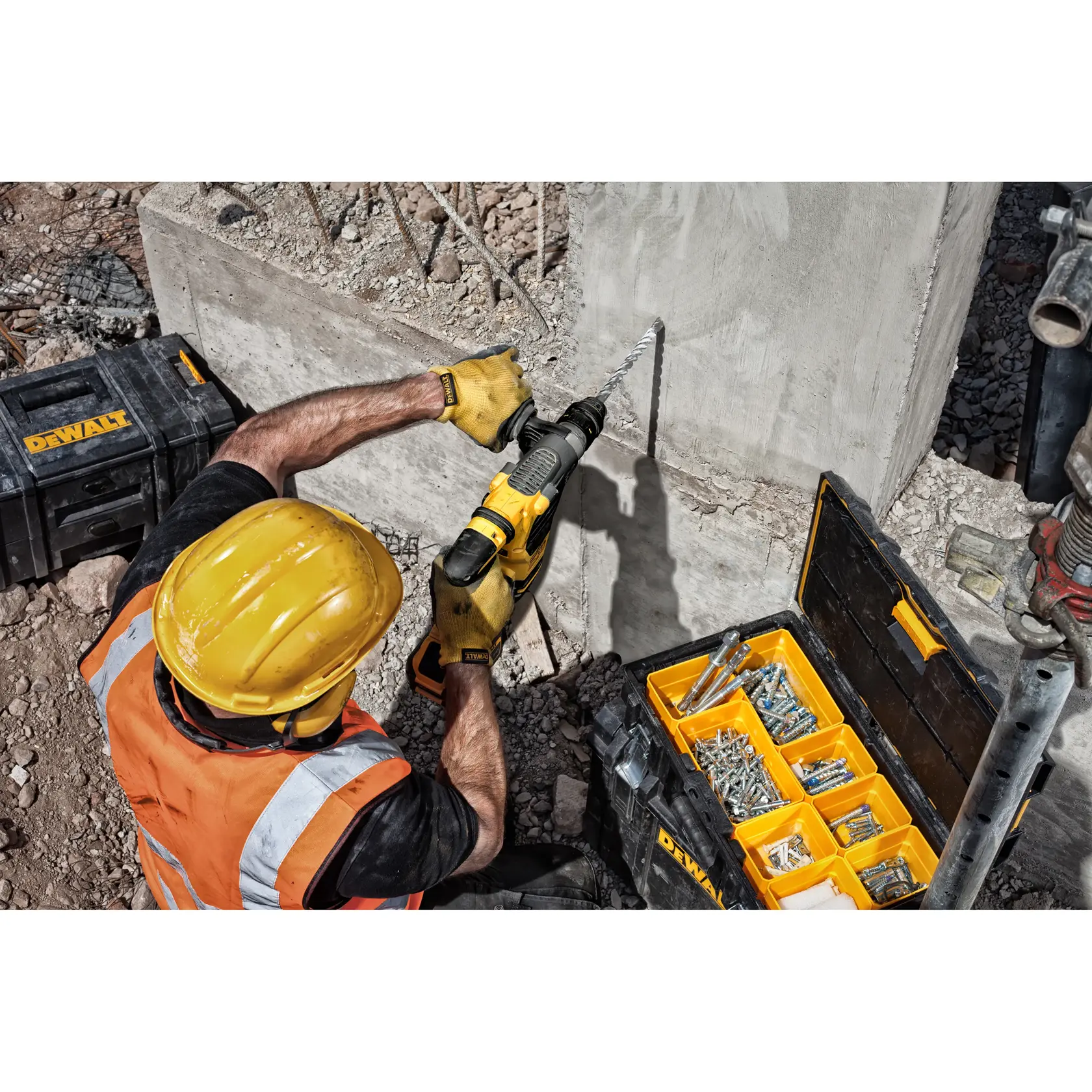 Trabajador taladra concreto con herramienta DEWALT, cajas y fijaciones DEWALT en obra.