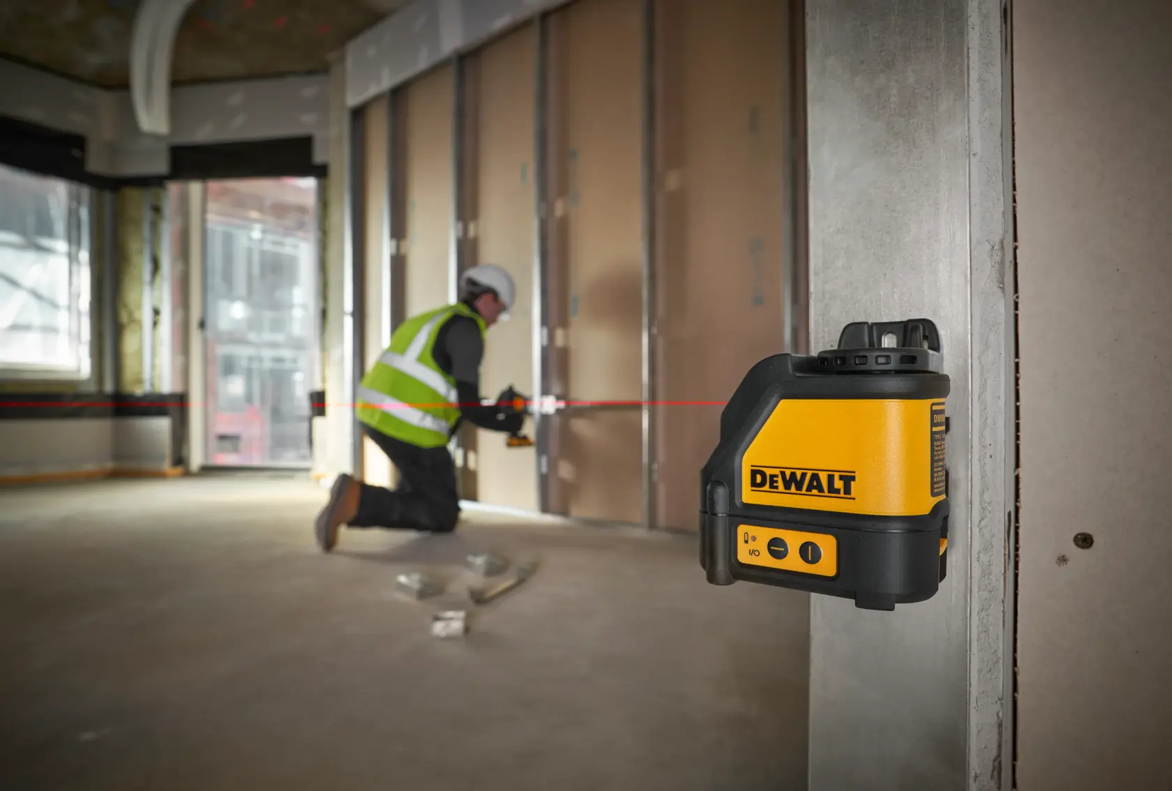 Worker using a DEWALT DW088K laser level on a construction site floor, wearing gloves and safety gear.