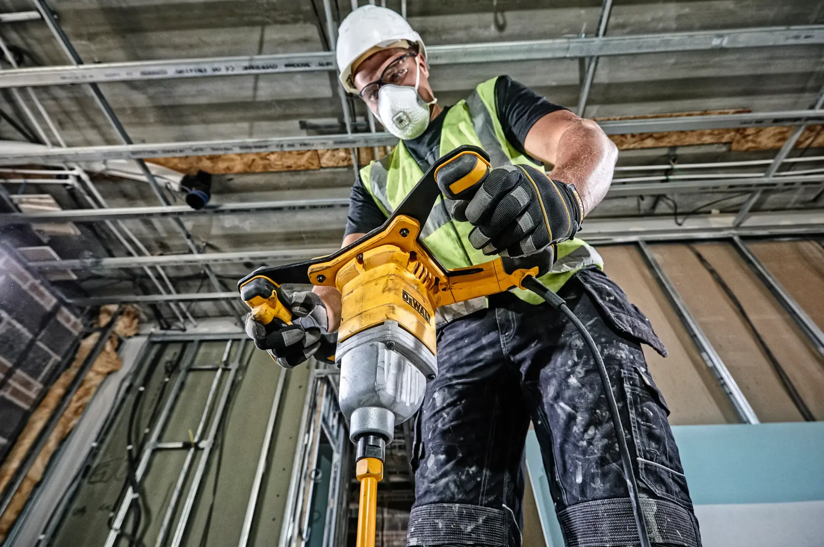 Persona usando mezclador DEWALT DWD241 en obra, vestida con chaleco y guantes de seguridad.