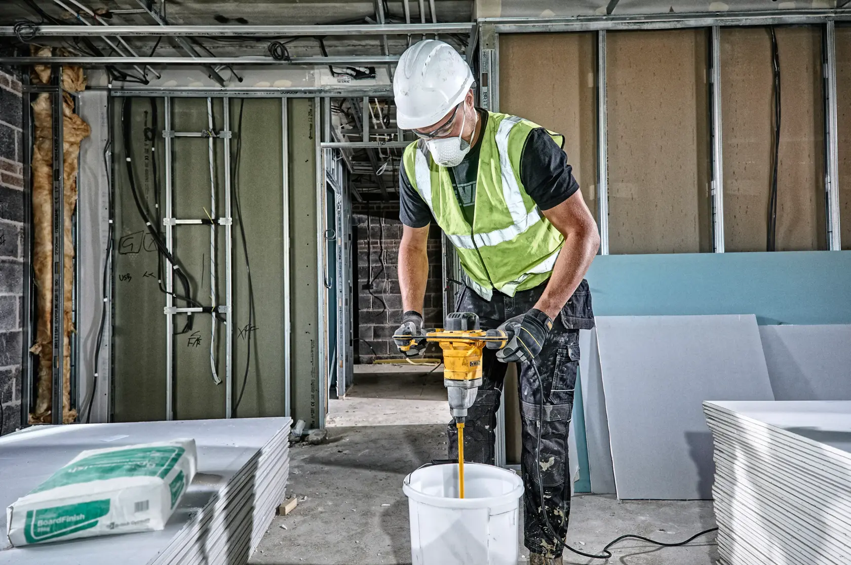 Trabajador mezcla materiales con taladro DEWALT DWD241 en un balde en obra de construcción.