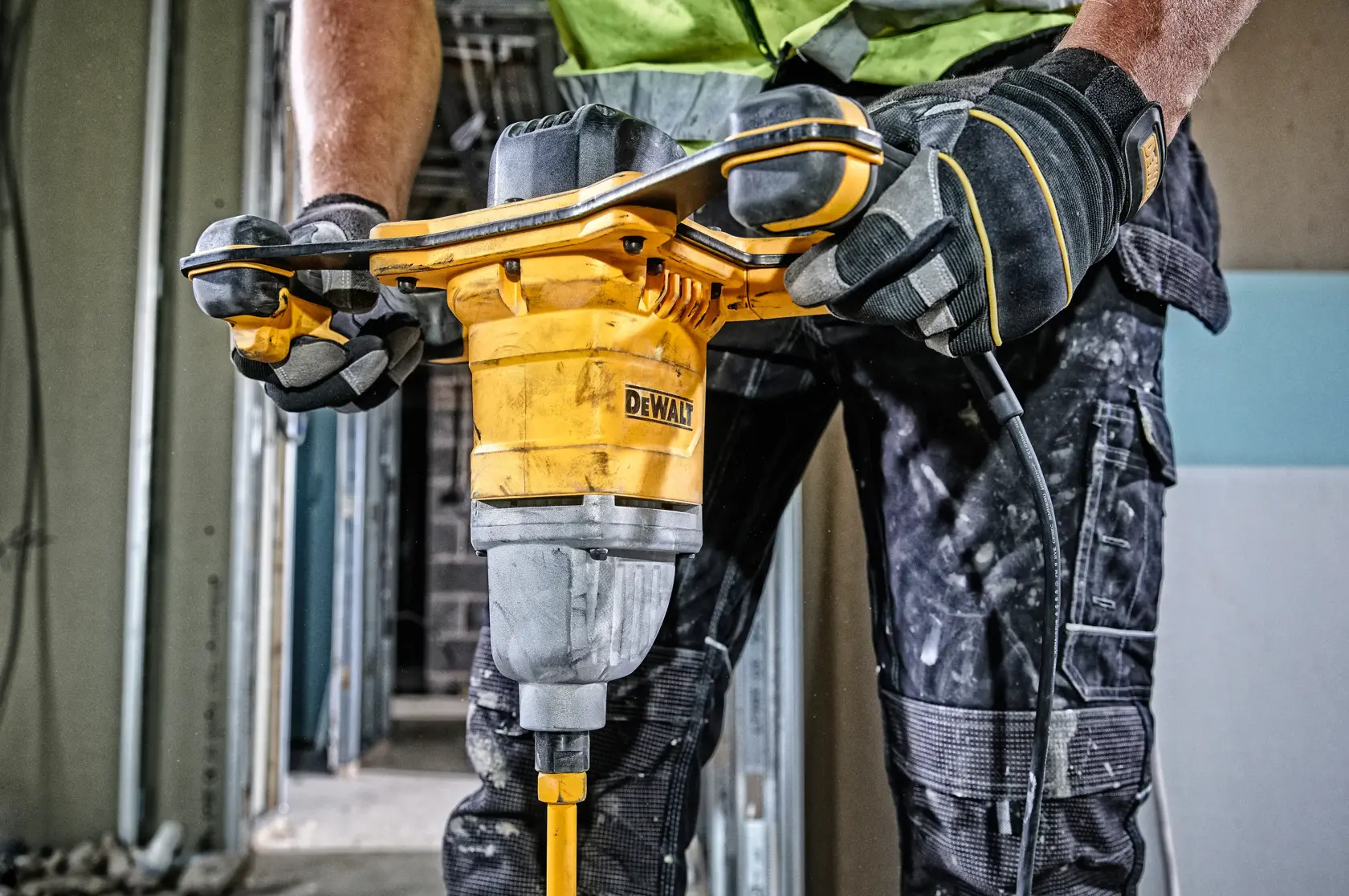 Persona usando mezclador DEWALT DWD241 en obra, con guantes y ropa de trabajo.
