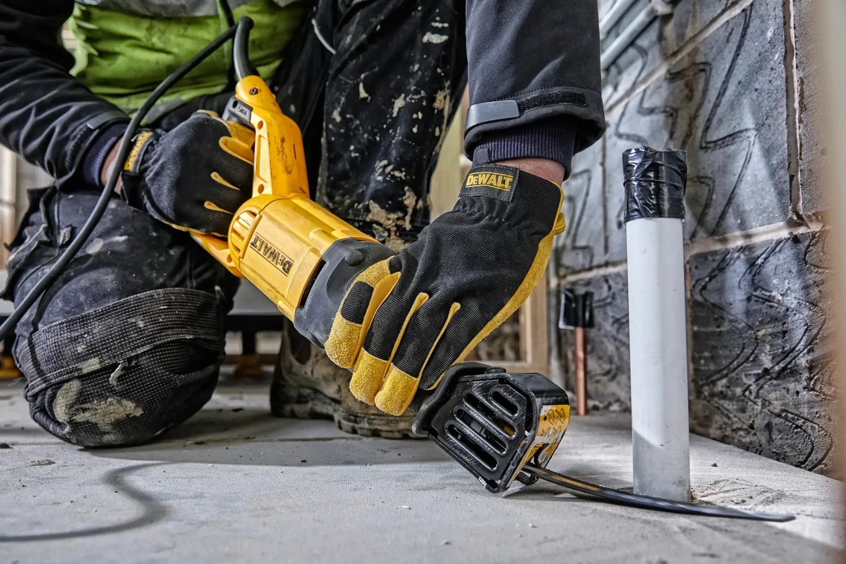Persona usa sierra DEWALT para cortar tubo en obra, lleva guantes y rodilleras.