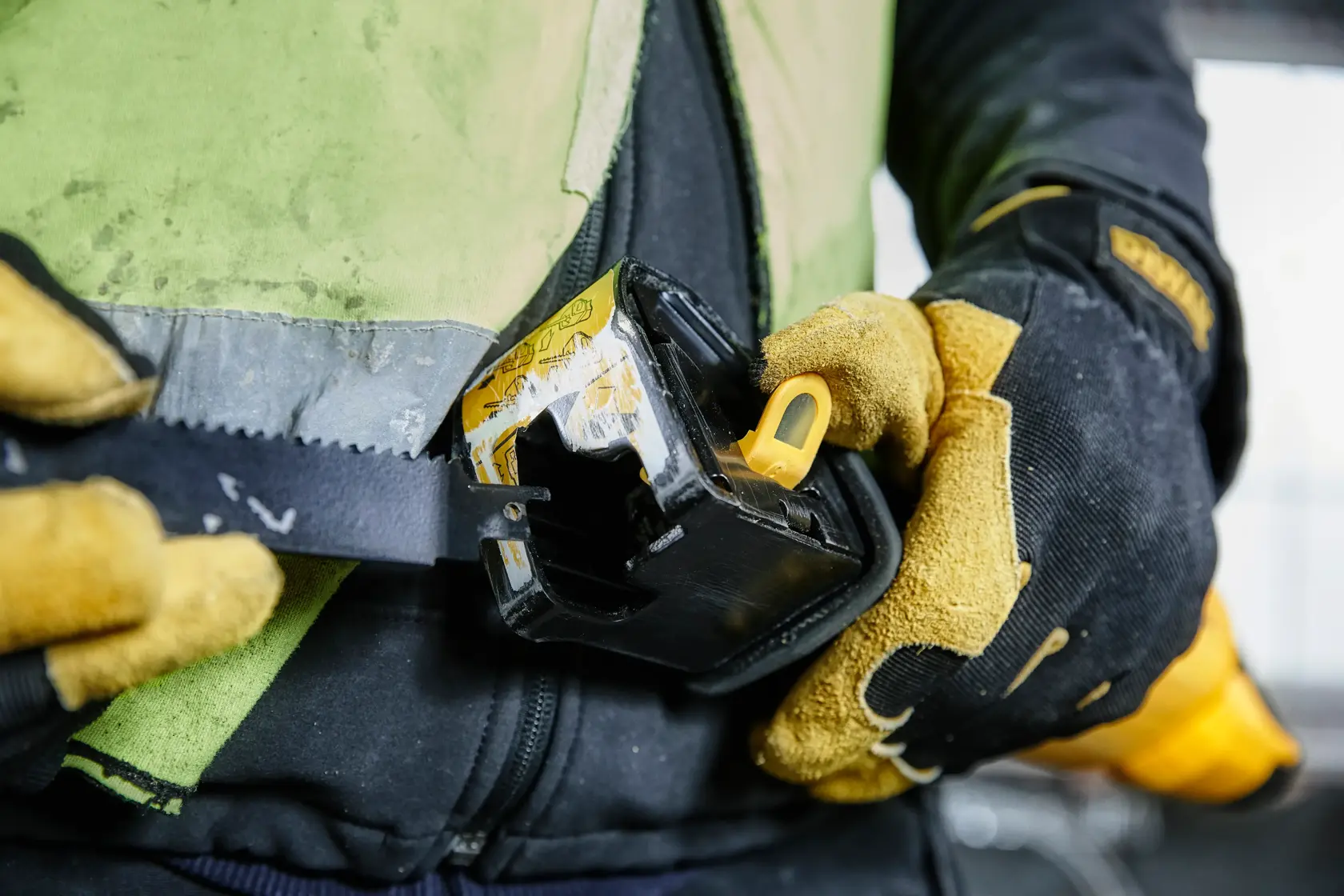 Manos enguantadas sujetan una herramienta DEWALT al cinturón, primer plano del equipo de trabajo.