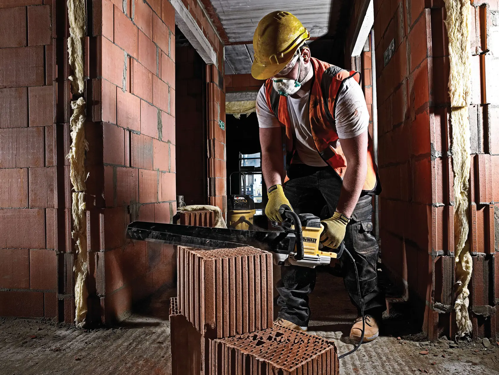 Arbeiter schneidet Ziegel mit DEWALT Säge auf Baustelle, trägt Schutzausrüstung und Handschuhe.
