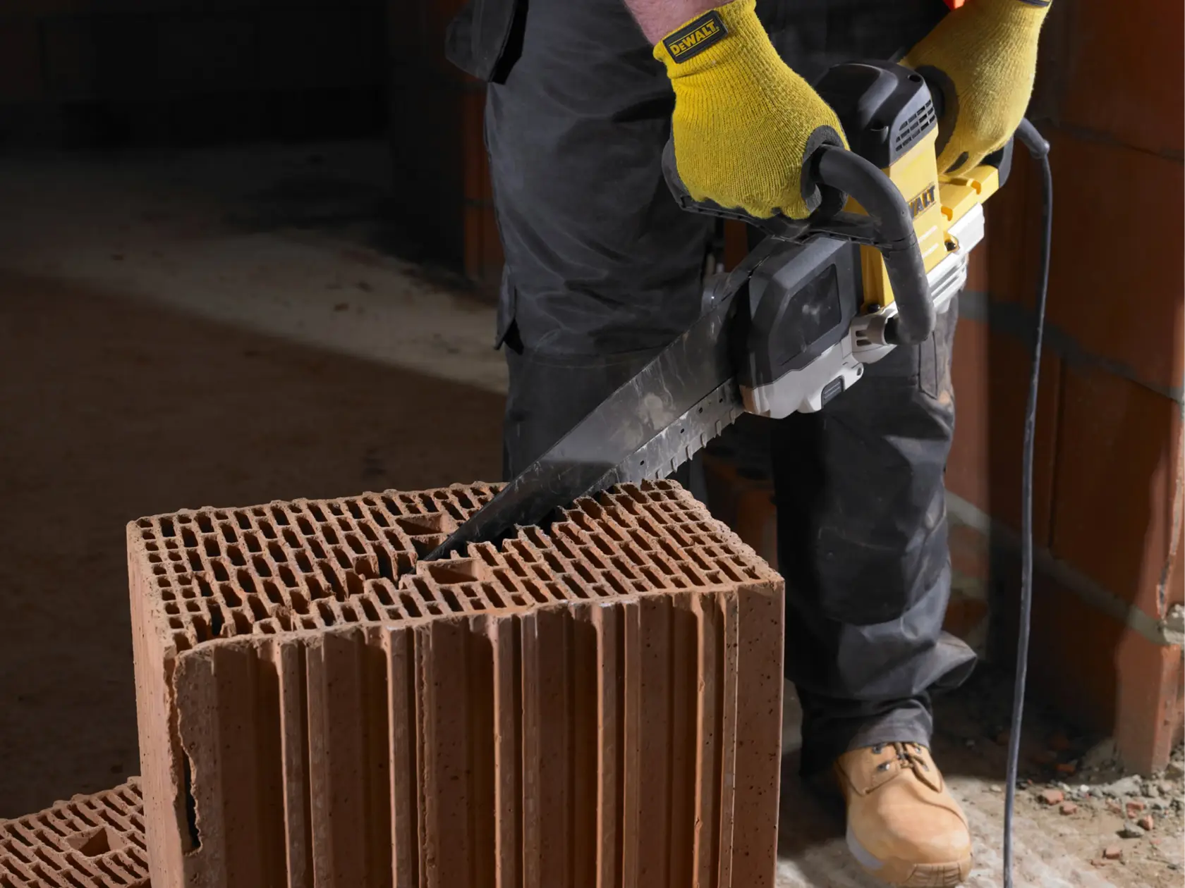 Person sägt mit einer DEWALT Säge einen hohlen Ziegel, mit Handschuhen, auf einer Baustelle innen.