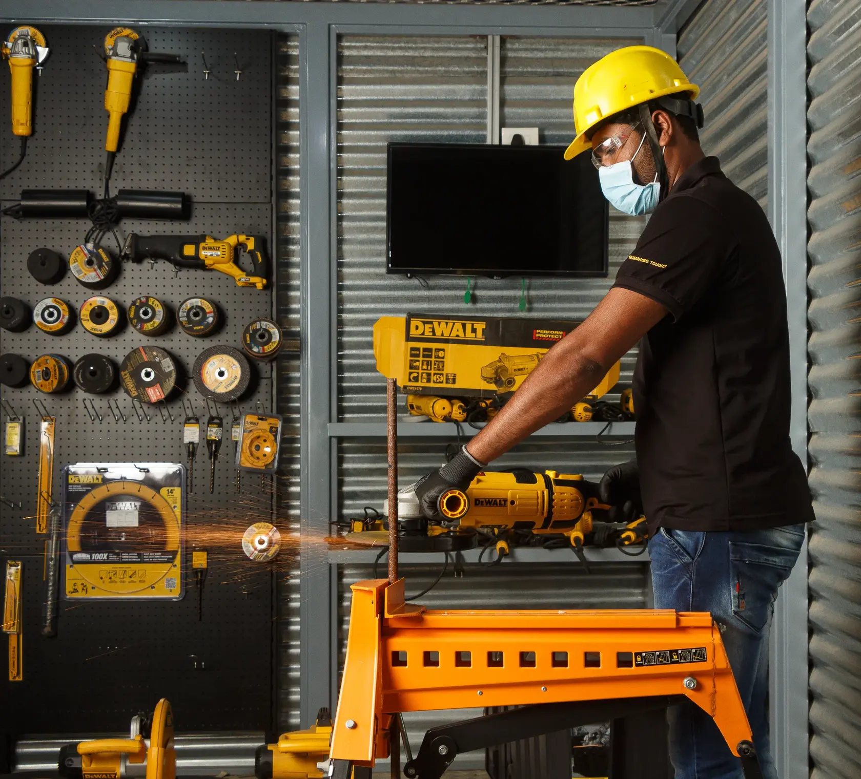 Photo of person using DEWALT DWE4579 grinder on metal rod in workshop with various DEWALT tools on display.