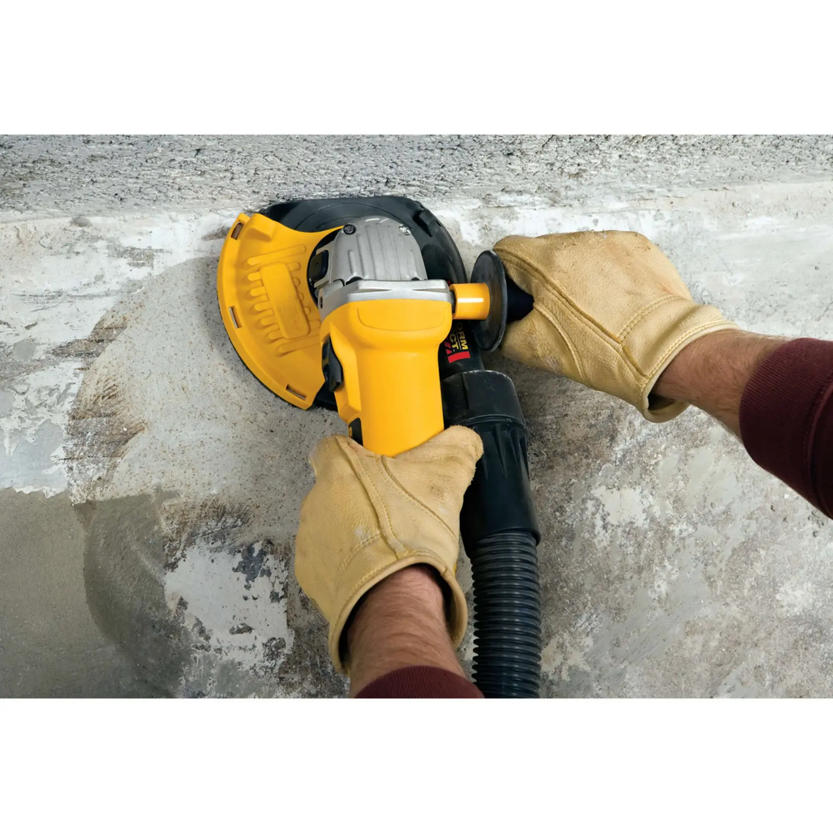 A construction worker wearing a yellow hard hat, gloves, and face mask is using a DEWALT DWE46150 surface grinding tool on a concrete floor, with a yellow DEWALT dust extractor vacuum in the background. The scene is set in an industrial or construction environment.