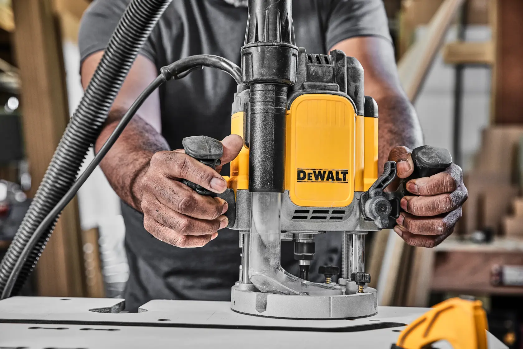Hands operate a DEWALT router tool on a workbench in a woodworking workshop.