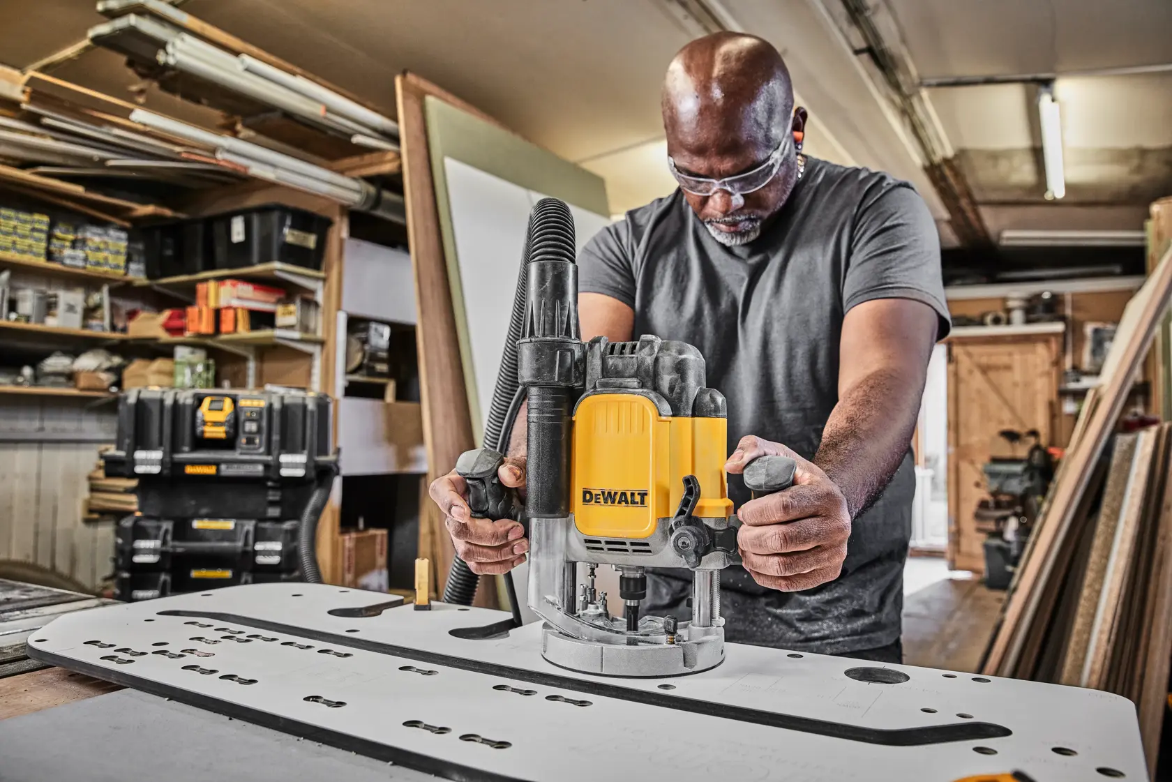 Person using a DEWALT DWE625KT router tool on a workbench in a workshop setting.