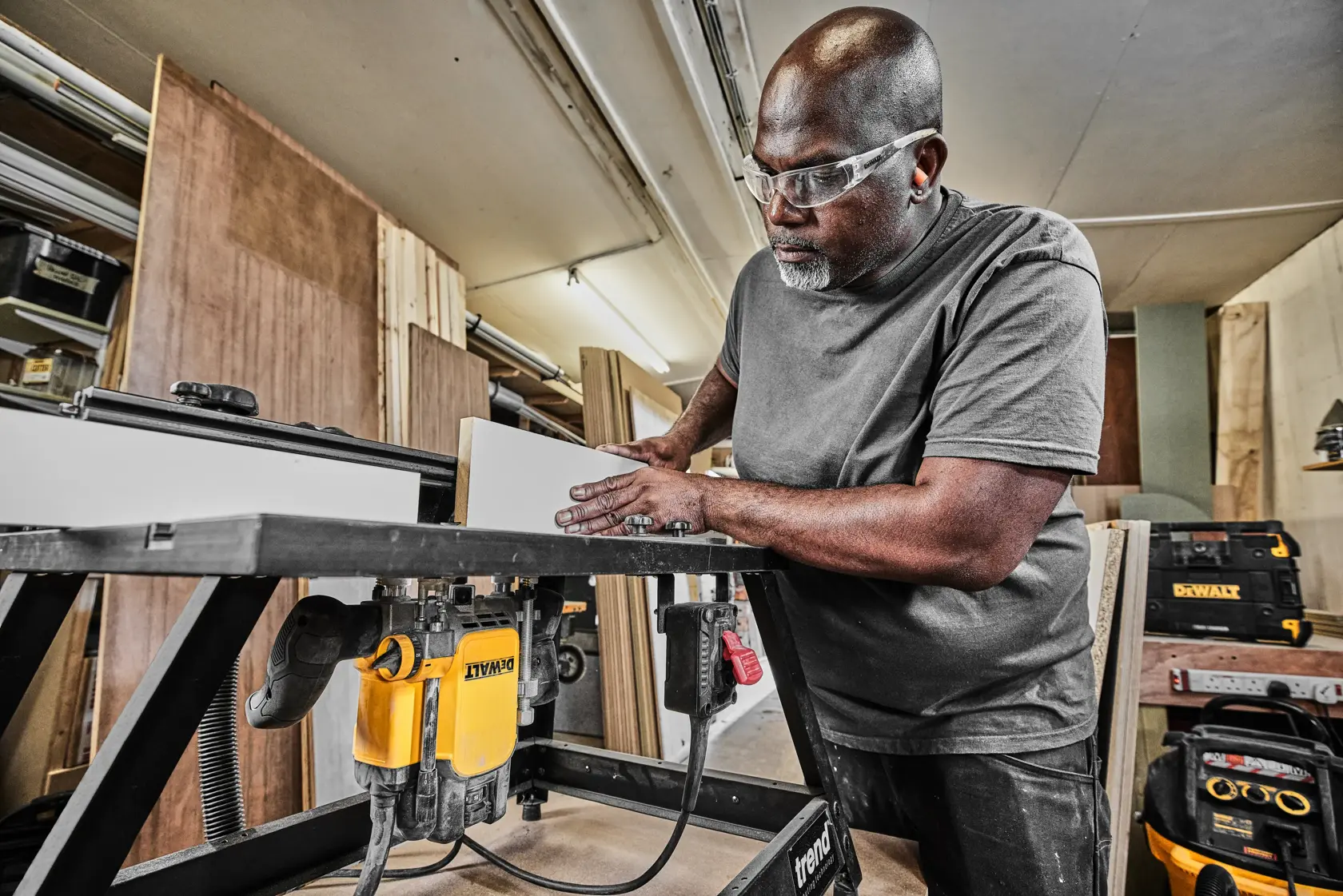 Persona usando una fresadora DEWALT DWE627KT en mesa de taller, cajas de herramientas al fondo.