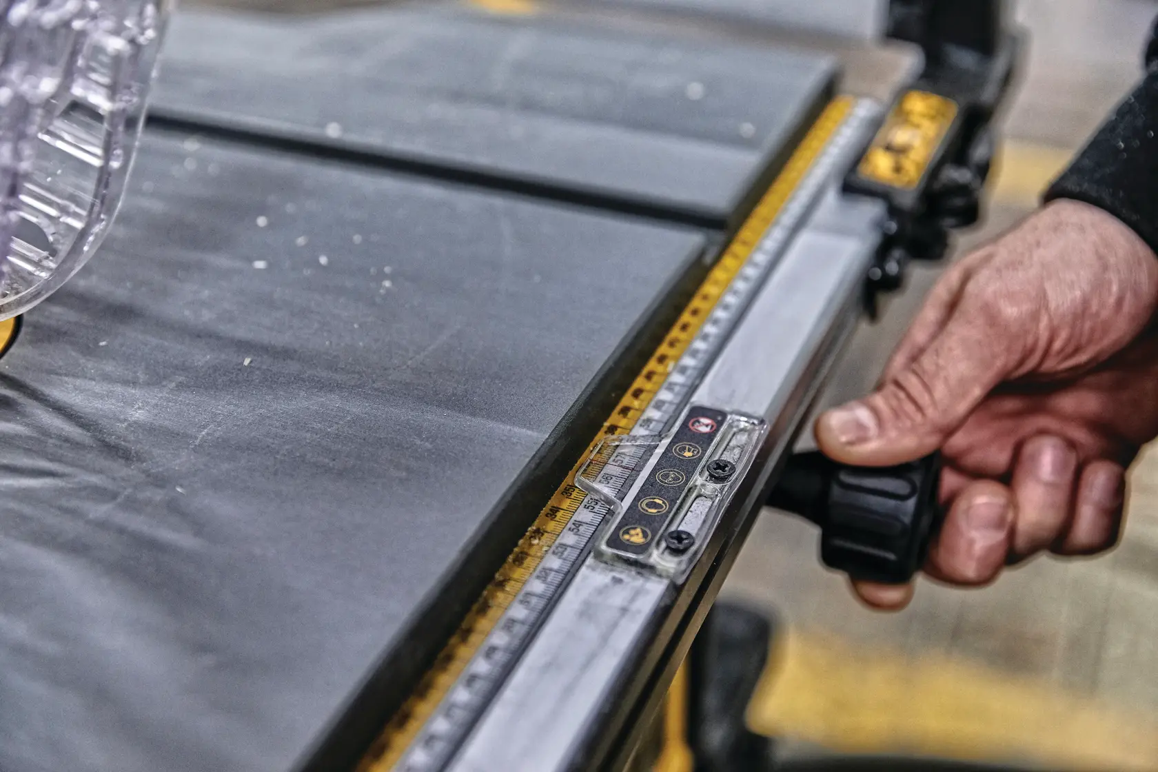 Primer plano de la mano de una persona ajustando la guía de una sierra de mesa DEWALT, mostrando la guía de medición y parte de la superficie de corte.