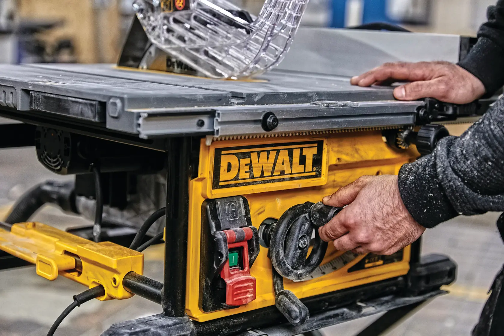 Primer plano de una persona ajustando la configuración de una sierra de mesa DEWALT, con un panel de control amarillo con interruptores y diales en un taller.