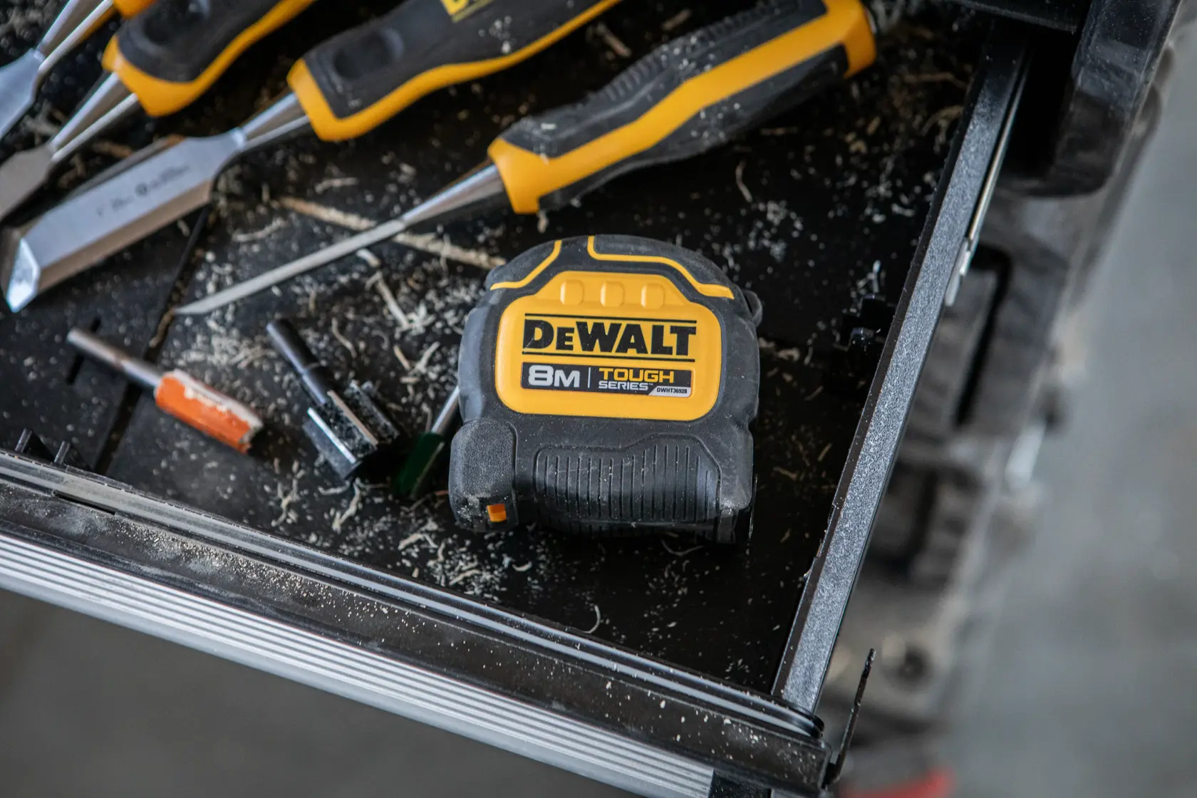 Cinta métrica DEWALT 8m en banco de trabajo con destornilladores y herramientas, rodeada de virutas.