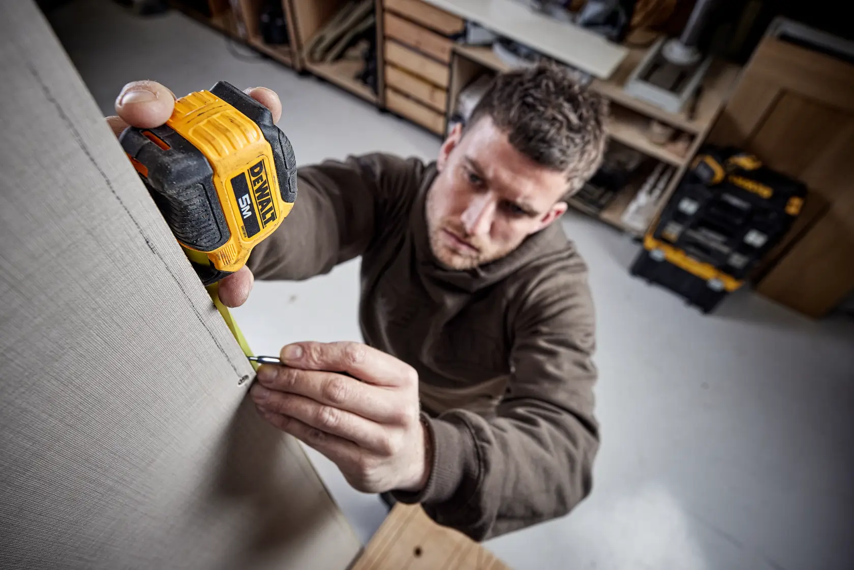 Persona mide una pared con cinta métrica DEWALT en taller. El rostro está desenfocado.
