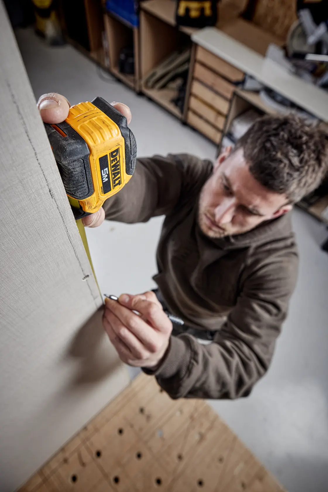 Persona usa una cinta métrica DEWALT de 5m para marcar medidas en una tabla vertical en taller.