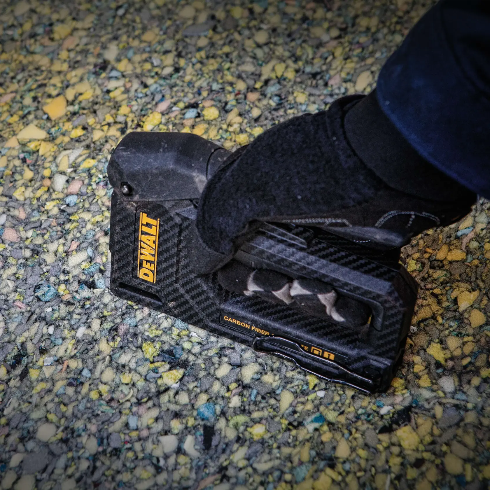 A person is using a DEWALT stapler, model DWHT80276, to secure a sheet of material to wooden framing at a construction site.