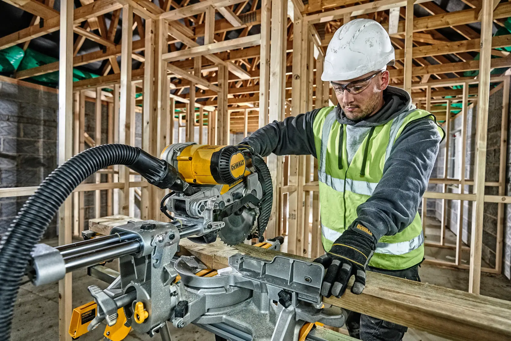 Arbeiter schneidet Holz mit einer DEWALT Kappsäge auf einer Baustelle, mit Schutzkleidung und Handschuhen.