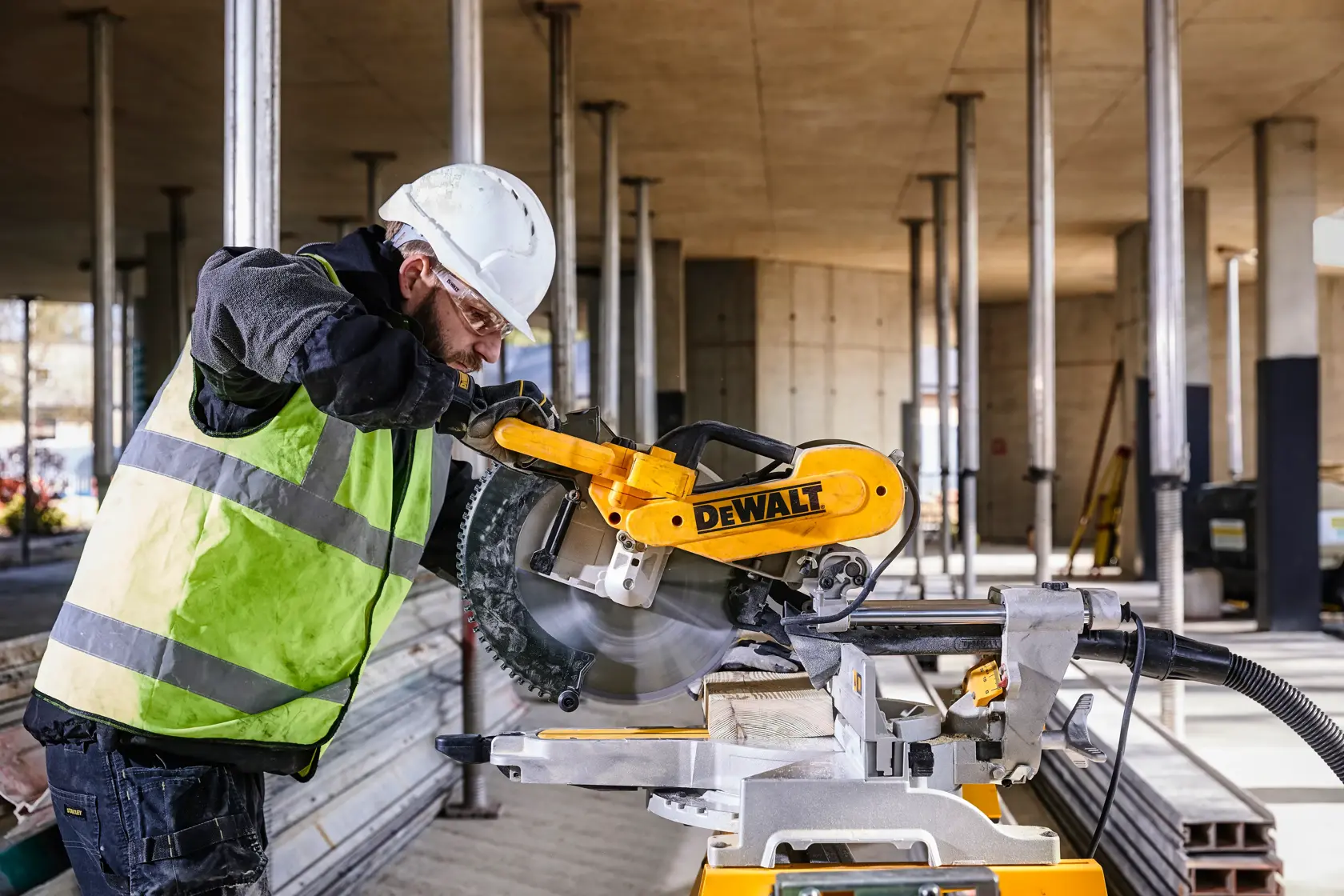 DEWALT DWS780, DWS780KIT saw in use at construction site, worker with helmet and vest. Photography category.