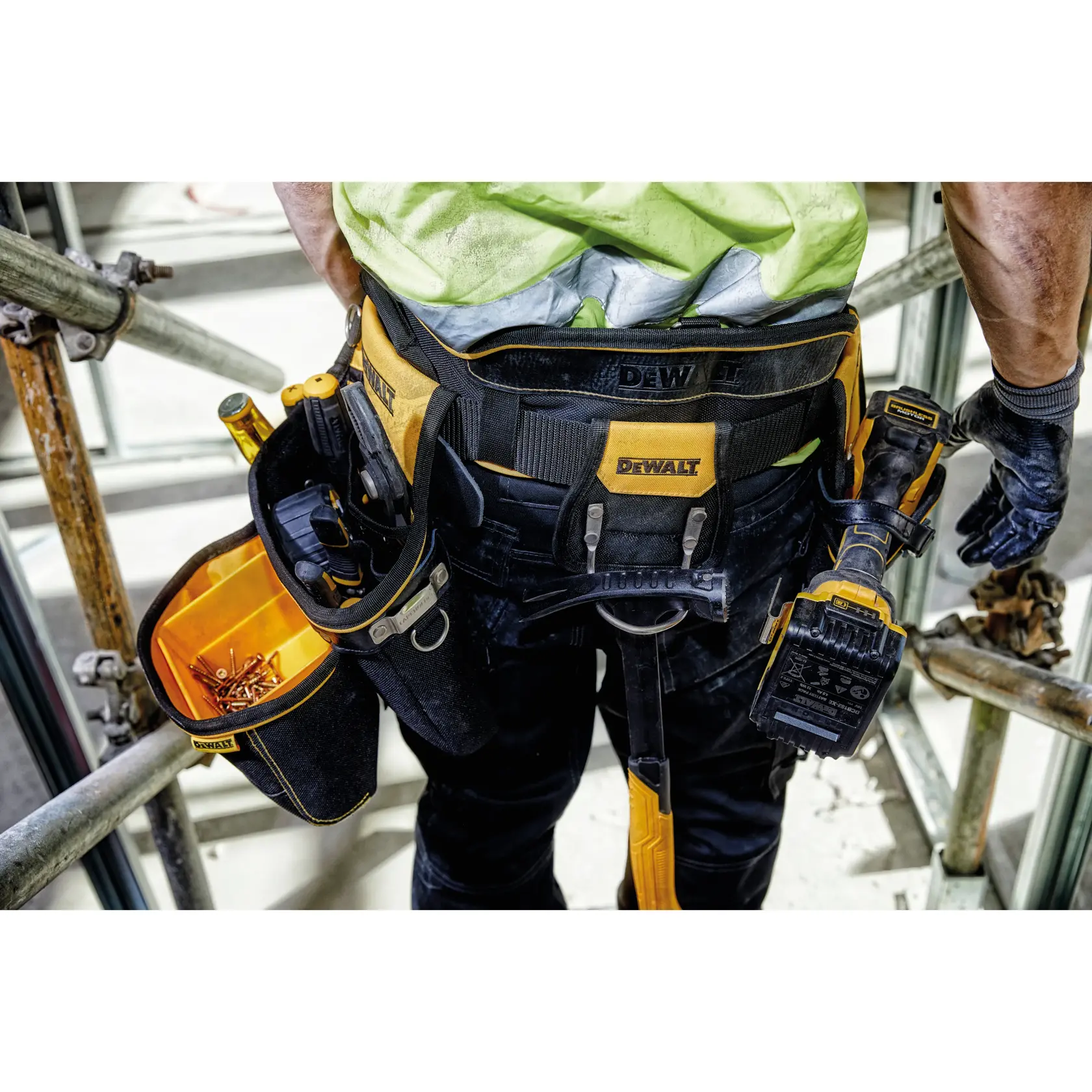 DEWALT tool belt worn by a worker, holding tools and screws, photographed at a construction site.