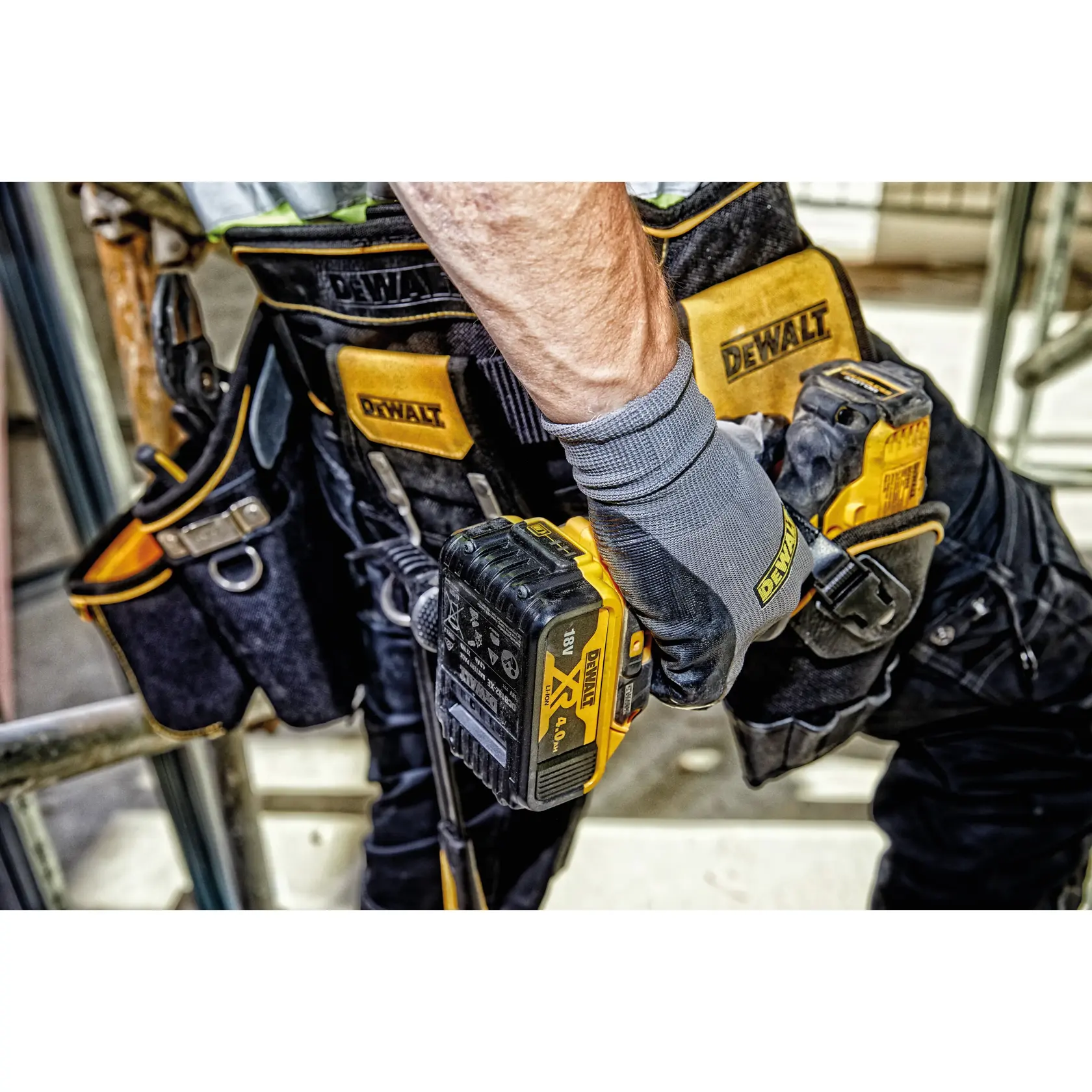Worker wears DEWALT tool belt and gloves, holding a yellow DEWALT drill at a construction site.